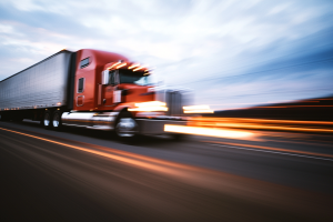 Red tractor-trailer barreling down the road, motion blur from high speed.