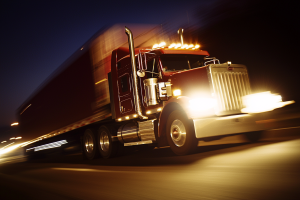 Red semi-truck with bright headlights moving at night, blurred background.