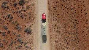 Groundbreaking 2025 Milestone: Kodiak Driverless Trucks Revolutionize Permian Oilfield Logistics 5 Aerial view of a red Kodiak-equipped truck hauling a trailer along a dusty lease road in a remote desert landscape.