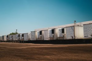 Refrigerated straight trucks parked in an industrial lot under a clear blue sky.