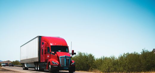 Red Class 8 semi truck hauling a trailer along a rural highway under daylight skies.