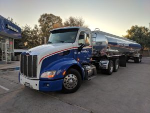 HM-265 Fuel Compliance: 7 Cost-Saving Changes—Efficiency Gains, Compliance Watchouts 3 Fuel tanker truck parked at a gas station with a flammable placard showing identification number 1203.