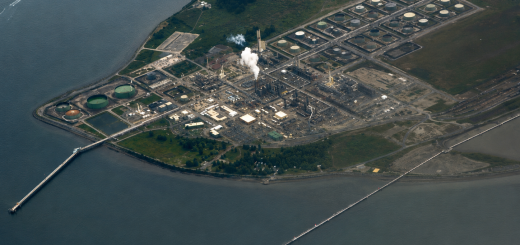 Aerial view of a waterfront refinery and storage tank complex illustrating how the global refinery crunch can affect refined product supply, fuel logistics, and downstream transportation markets.