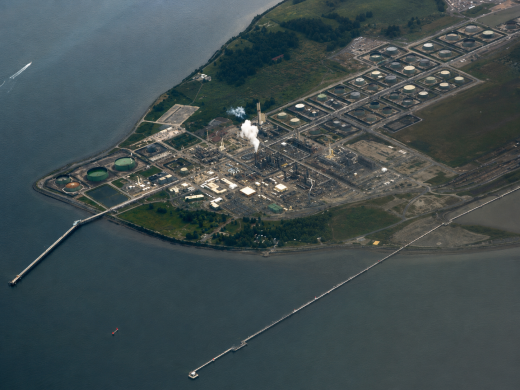 Aerial view of a waterfront refinery and storage tank complex illustrating how the global refinery crunch can affect refined product supply, fuel logistics, and downstream transportation markets.