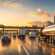Operation Safe Driver Week 2026 highway traffic scene with a tanker truck, bus, van trailer, and passenger vehicles traveling on a wet city freeway at golden hour