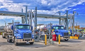 Renewable Diesel Mandate Reality Check: 7 Critical Pressures Facing U.S. Fuel Markets 15 Two tanker trucks positioned at a fuel-loading terminal with overhead piping and transfer equipment.