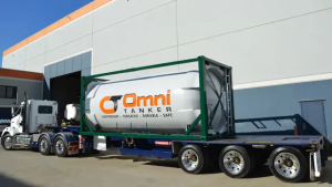 PHMSA Tank Special Permits Put Composite Portable Tanks and MC 331 Design to the Test 2 White Omni Tanker composite tank container in a green frame mounted on a semitrailer outside an industrial building