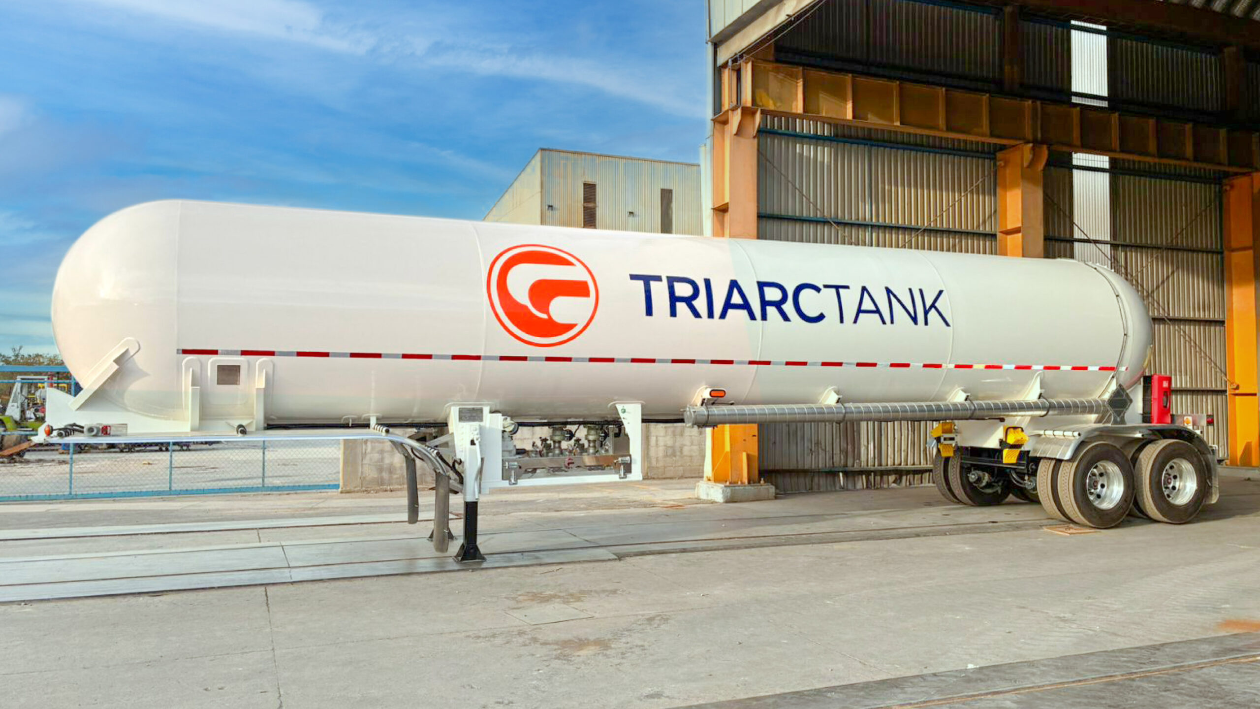 White TriArc MC 331 LPG tank trailer with tandem axles parked outside a manufacturing building.