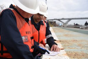 Coast Guard Proposes Nationwide Tank-Barge Inspection Flexibilities 5 Two Coast Guard officials in hard hats reviewing printed documents on a barge deck
