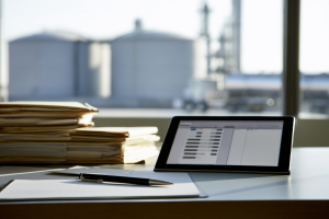 EPA Exempts 1.76 Billion RINs, Extends 2025 RFS Deadline to October 1 2 Tablet displaying an abstract compliance ledger beside paper files, with fuel storage tanks and a tanker blurred in the background