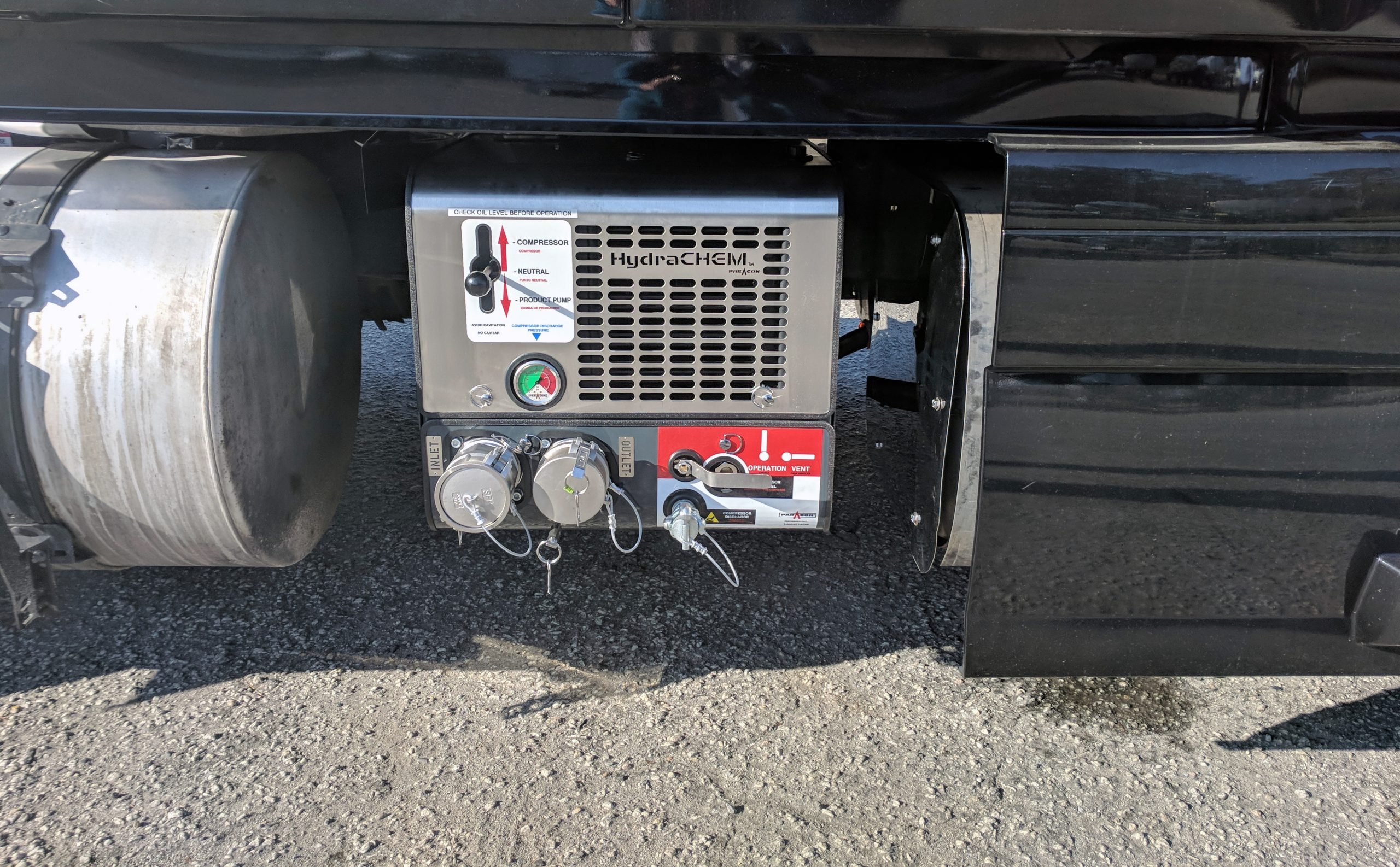 Paragon HydraCHEM system mounted beside a truck’s fuel tank, with controls, a pressure gauge, and capped hose connections visible.