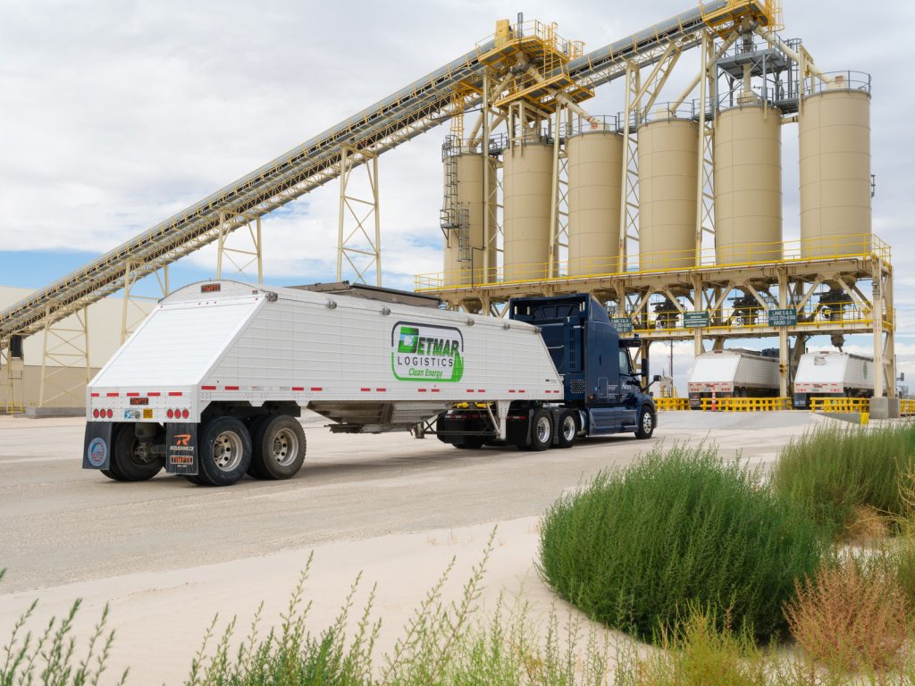 FMCSA’s Driverless-Truck Beacon Exemption Covers Tankers but Excludes Hazmat 10 Aurora-equipped tractor and Detmar Logistics hopper trailer beside silos at a bulk loading facility.