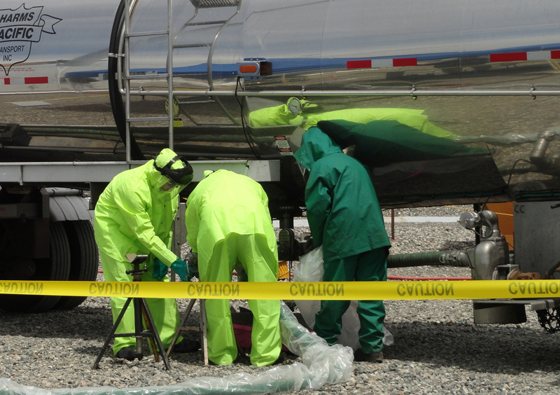PHMSA Clarifies Organic-Peroxide Tank Limits and Caustic-Soda Residue Rules 4 Workers in protective clothing handle transfer equipment beside a caustic-soda tanker at the Hanford Site.
