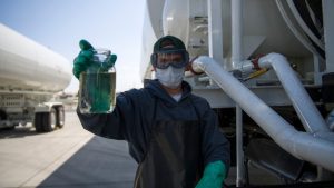 Stephens Pneumatics Selected to Supply Military Agile Fuel Systems 6 Fuel operator holds a clear jar of jet fuel beside the piping and hose reel of an aircraft refueler.